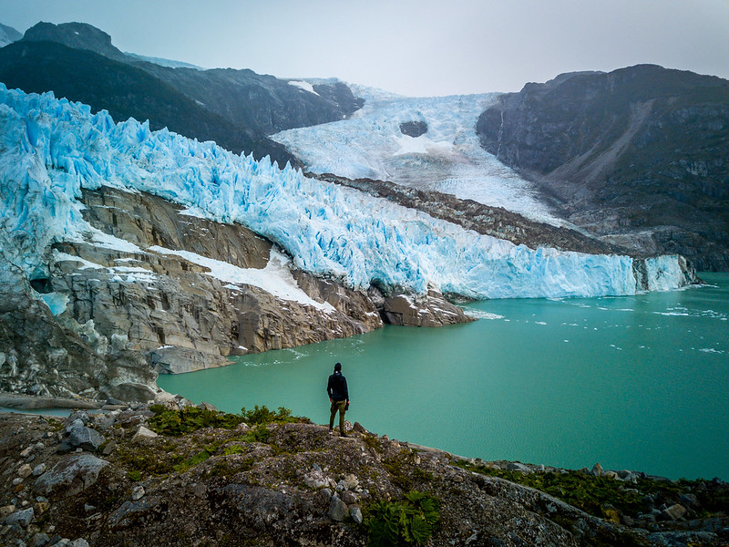 A hiker admires a sapphire-blue glacier and peppermint glacial lake