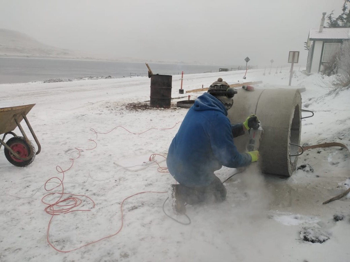 A male worker cuts a concrete pipe in the snow