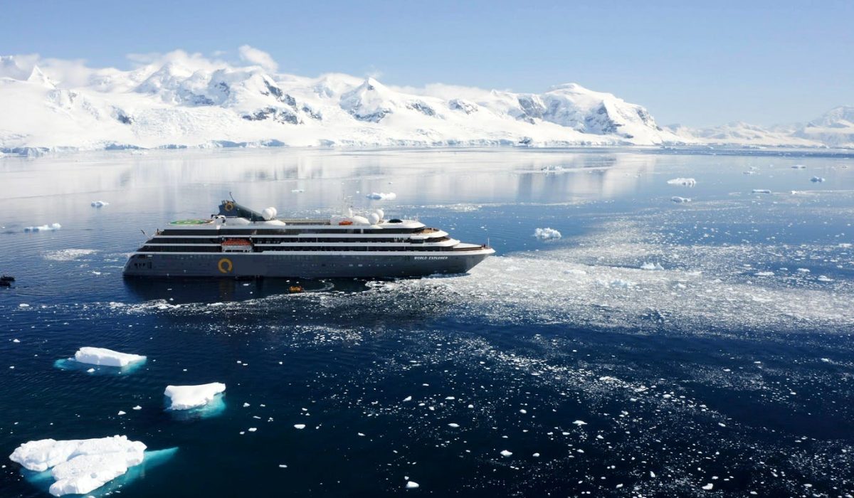 An expedition ship in Antarctica surrounded by snowy mountains and icebergs