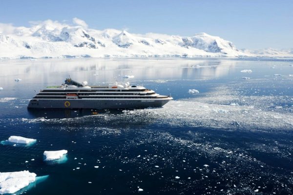 An expedition ship in Antarctica surrounded by snowy mountains and icebergs
